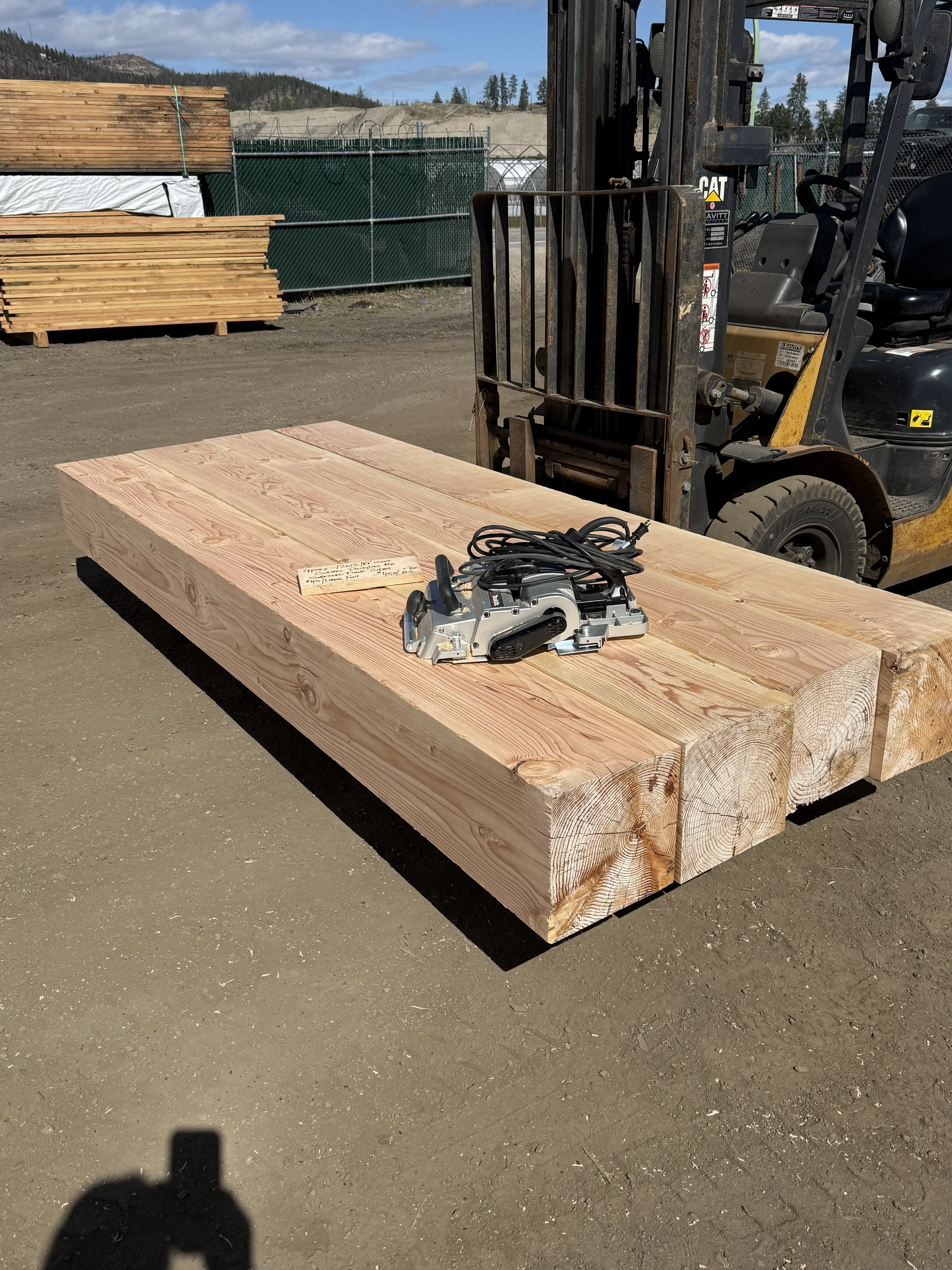 Large timber tabletop being planed in the yard with CAT forklift in the background