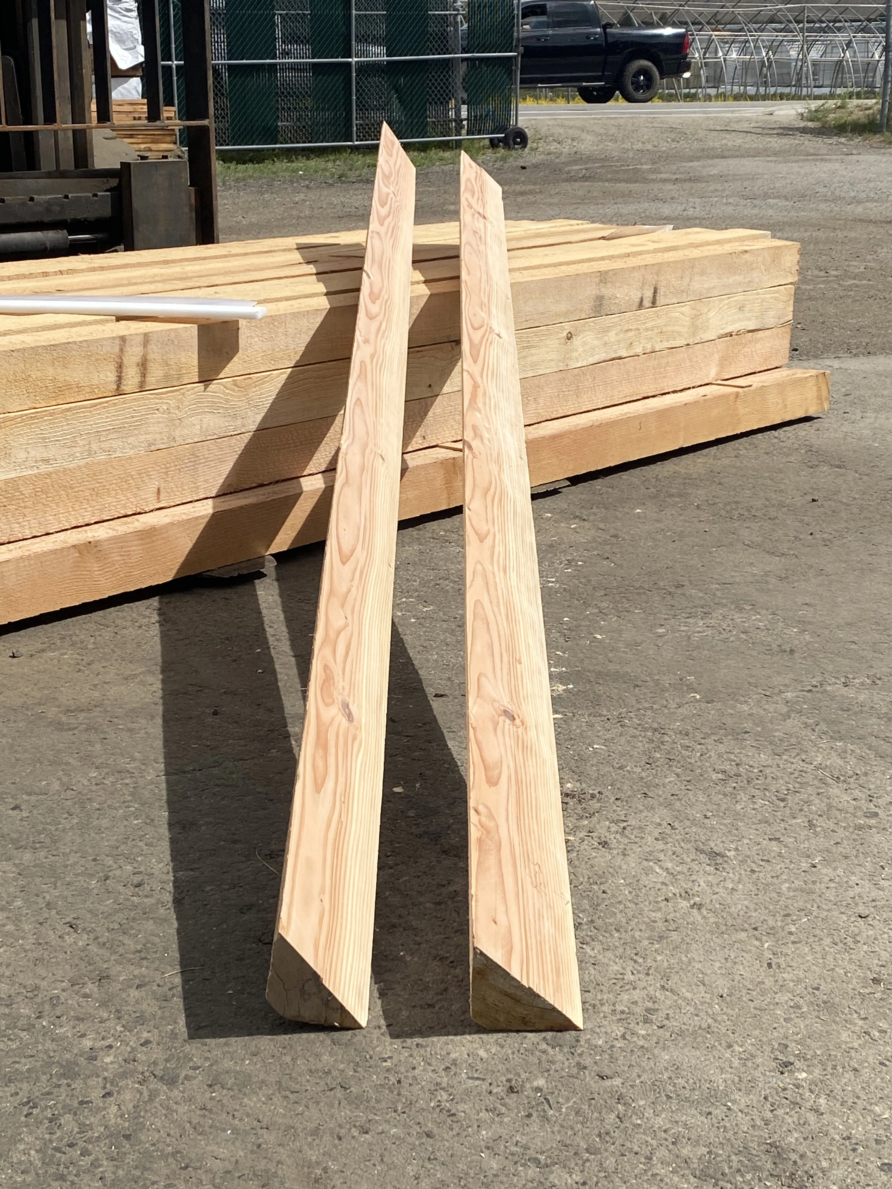 Two freshly cut cedar planks standing upright against stacked lumber in the yard